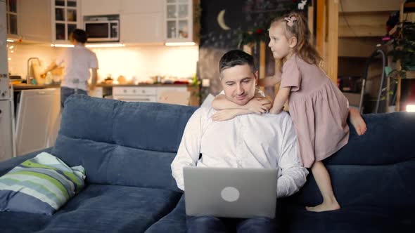 Dad Is Trying To Work on Laptop with Two Children Cuddling Him in Living Room