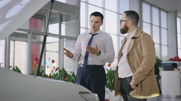 Sales Manager and Client Near a New Car with an Open Hood alt