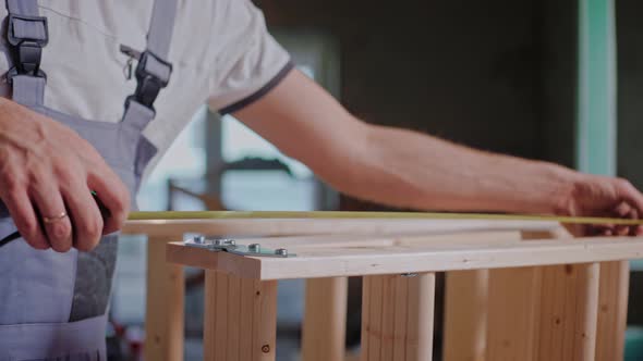 Male Builder Uses a Tape Measure to Measure Wood Construction in the Studio