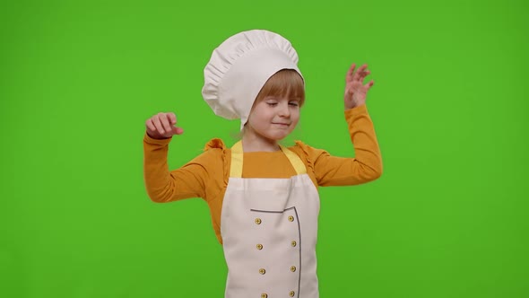 Child Girl Kid Dressed in Apron and Hat Like Chef Cook Baker Raising Hands Showing Tasty Gesture alt