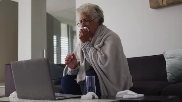Sick african american senior woman coughing while having a video call on laptop at home alt