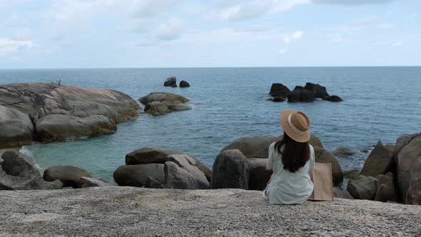 Rear view of a young woman sitting on the rock by the sea