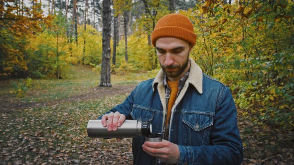 Young Caucasian Man Tourist Pouring Tea From Thermos Enjoying It and Autumn Nature During Travel in alt