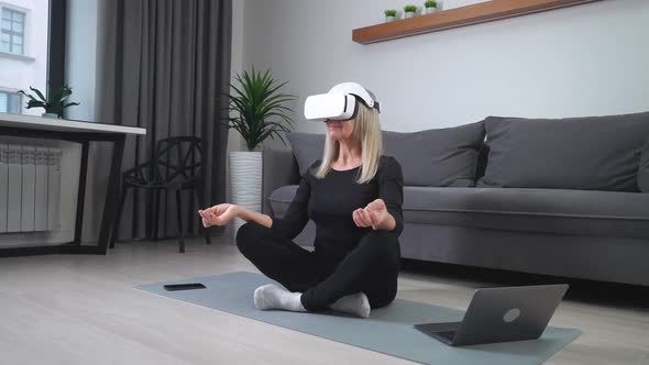 Cheerful Elderly Woman in Virtual Reality Glasses Meditates in the Living Room Modern Technology and alt