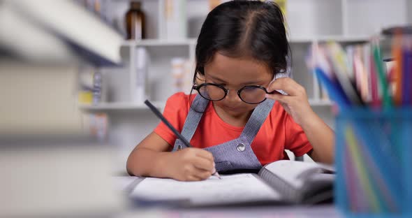 Little girl wearing glasses practicing writing worksheet at the desk at classroom. alt