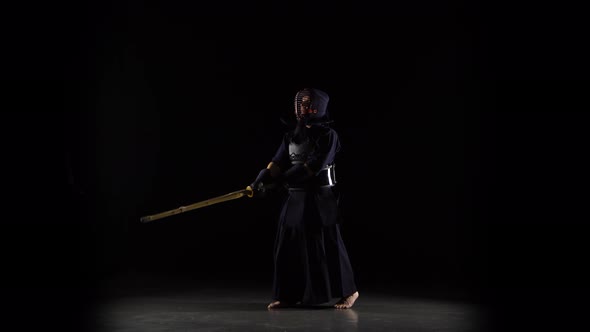 Strong Kendo Guru Practicing Martial Art with the Bamboo Bokken on Black Background. alt