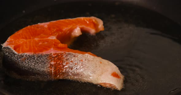 Piece of salmon fish frying on hot pan with sizzling oil at home kitchen