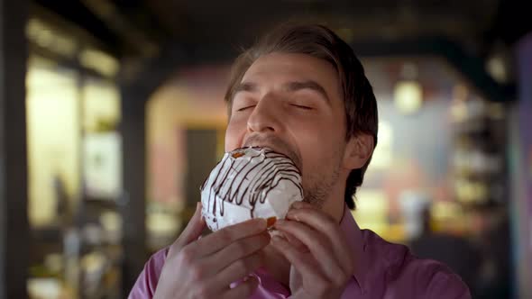 Closeup of a Handsome Man Enjoying a Cake with Icing Greedily Bites It and Smiles alt