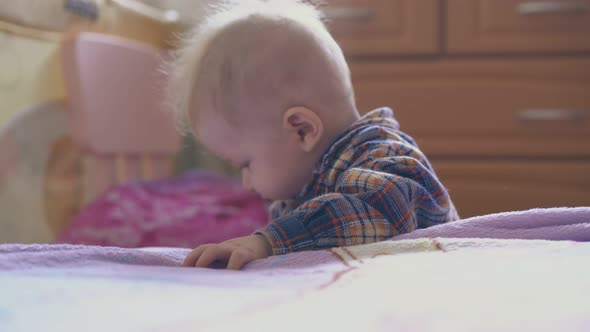Little Baby in Shirt Nibbles Plastic Tube at Bed in Room alt