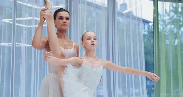 Teacher Helps Girl Raise Leg Standing Near Window in Studio alt