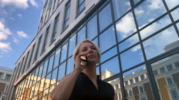 Business Woman is Talking on Phone Against the Backdrop of Glass Business Center