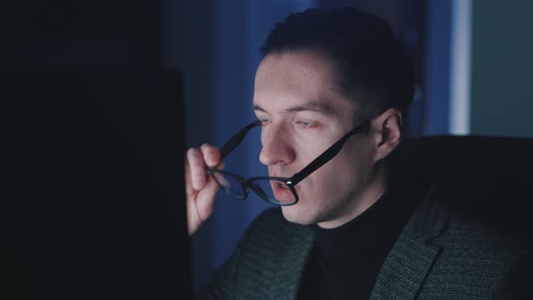 Afraid and Shocked Man Looking at Monitor Screen Takes Off Glasses and Cover His Mouth with His Hand alt