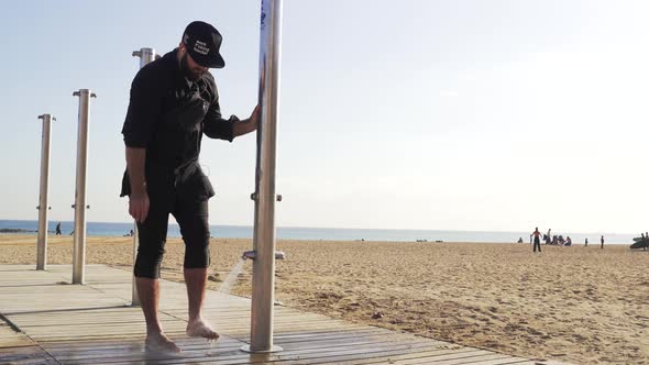 The guy washes his feet from the sand in the shower near the beach