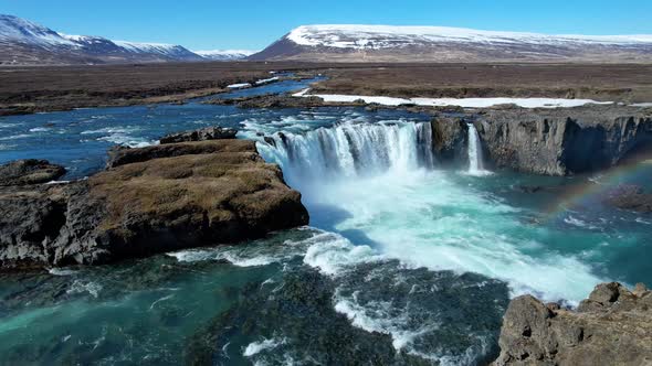 Godafoss Waterfall  in Northern Iceland with snow capped mountains and rainbow alt
