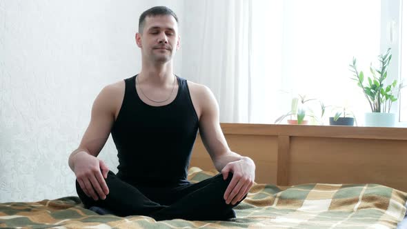 Young Attractive Man Performing Assanas Sitting on the Bed in His Living Room
