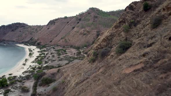 Aerial drone flying over a rugged, dry, brown hilly landscape volcanic looking terrain during dry se alt