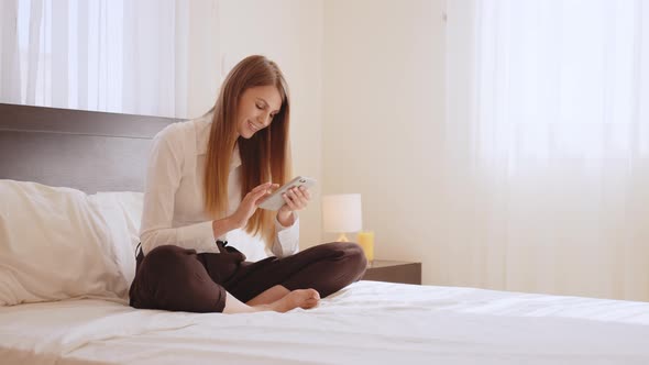 Pretty Caucasian Woman Sitting on Bed with Crossed Legs and Using Modern alt