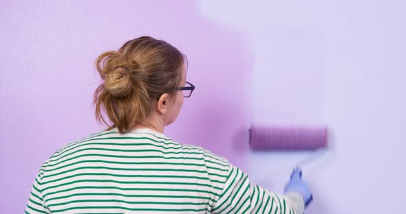 Young Woman with Glasses and Working Rubber Gloves Repaints Wall in the Room in Darker Shade Rolls a