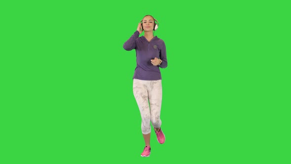 Sporty Woman Listening Music in Headphones While Running on a Green Screen Chroma Key alt