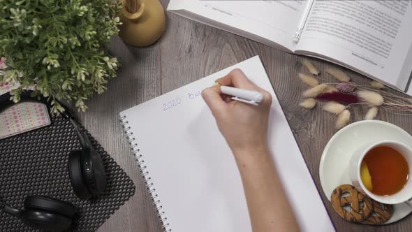 View From Top: Girl's Hand Writes Bucket List on New 2020 Year, Writes with Pen