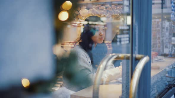 Young Asian Woman is Looking at the Street While Drinking Coffee Alone in Cafe