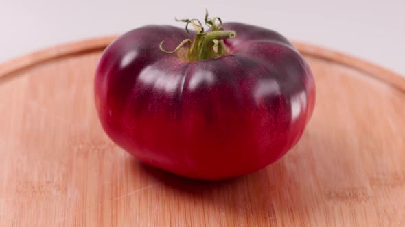 Close up view of ripe black variety of tomato on wooden cutting board isolated in background. alt