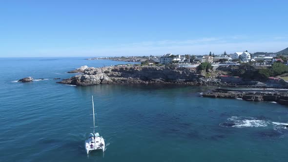 Drone shot passing and pulling away from a cruising catamaran next to cliffs in ocean alt