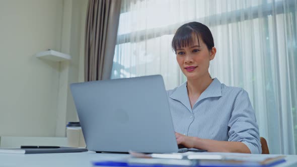 Asian attractive happy business woman sit on working table, turn on laptop computer in office. alt