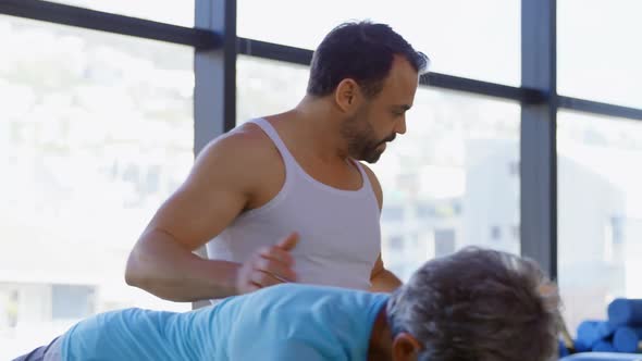 Trainer assisting senior women in performing yoga 4k alt