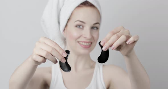 Young Woman with Towel on Head After Shower Holding in Hands Two Black Under Eye Patches alt