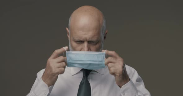 Professional middle-aged businessman wearing a surgical mask and looking at camera