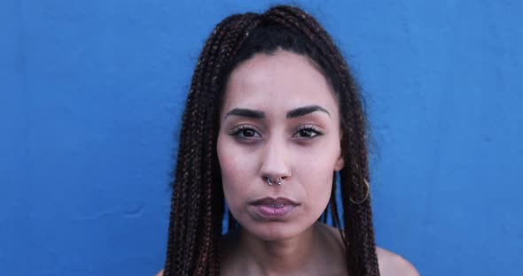 Mixed race girl looking serious on camera with blue background alt