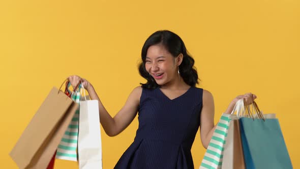 Happy beautiful Asian young woman holding colorful shopping bags