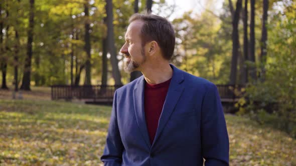 A Middleaged Handsome Caucasian Man Walks and Looks Around with a Smile in a Park in Fall