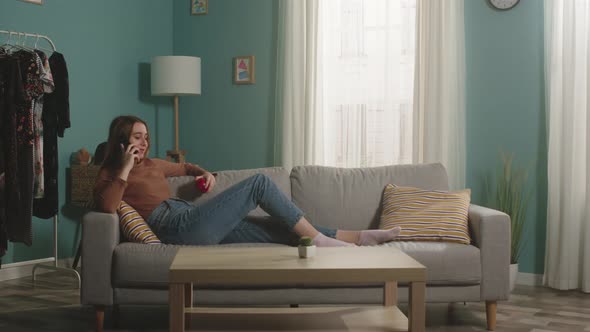 Young Lady with Red Apple Lies on Sofa and Talks on Phone