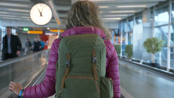 Blonde Woman with Backpack Rides on People Mover at Airport alt