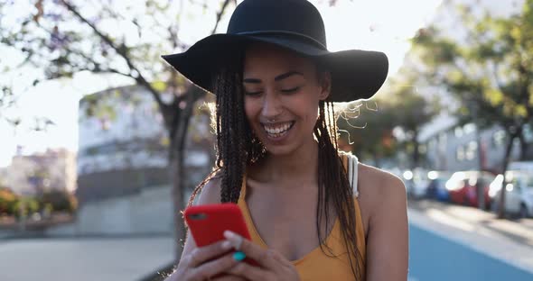 Bohemian mixed race girl using smartphone outdoor with city in background alt