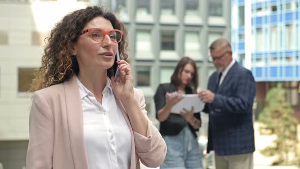 Portrait of a Middleaged Businesswoman Talking on a Mobile Phone in the Courtyard of a Large alt