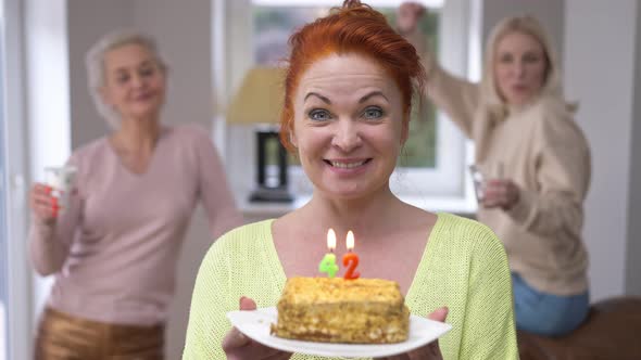 Joyful Redhead Beautiful Woman with Birthday Cake Blowing Out 42 Years Candles Smiling Looking at alt