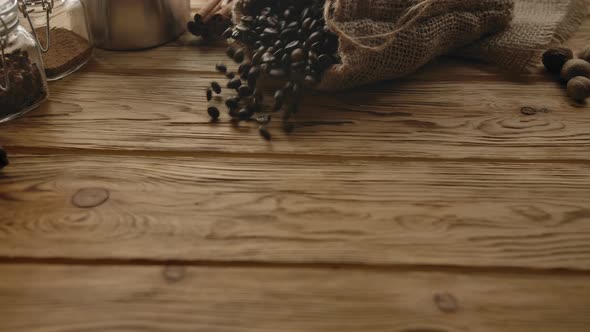 Roasted Coffee Beans Falling Down with Jute Sack on Wooden Table alt
