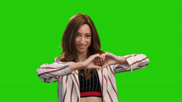 Cute smiling girl pose on green screen showing heart and thumb up gestures alt
