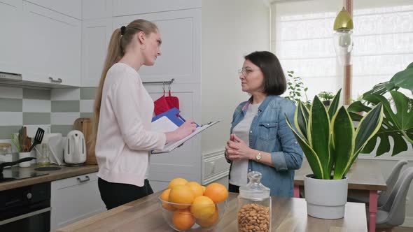 Young Employee Talking with Mature Woman and Writing Survey Interview alt