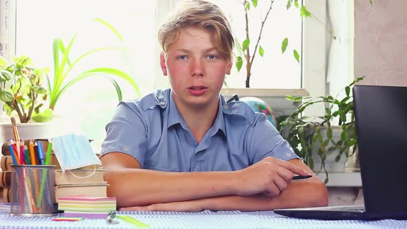 Young Teenager in a Blue Shirt European Appearance Sits at a Work Table  alt
