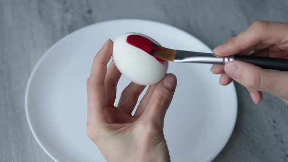 Close-up. Female hands paint Easter egg in a modern minimalist style with colorful paint.