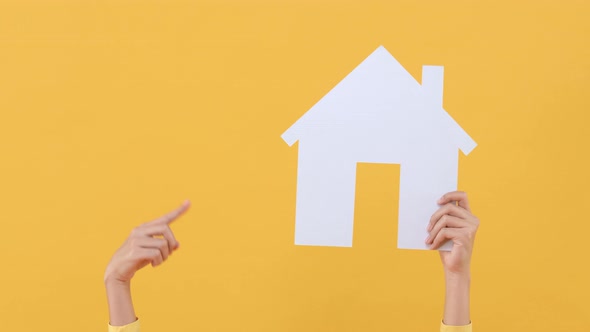 Hand raising and pointing to house model isolated on yellow background