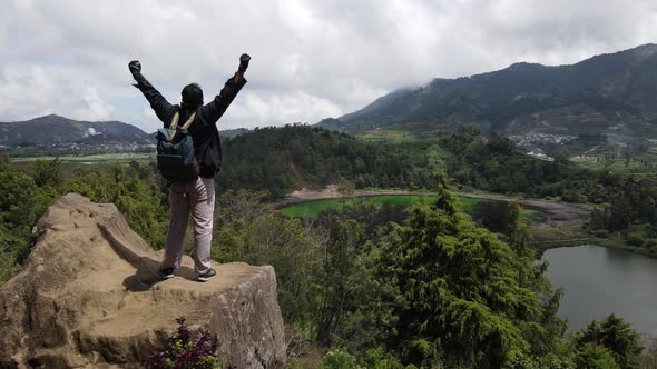 Young man standing on a rock of a cliff and enjoying the view alt