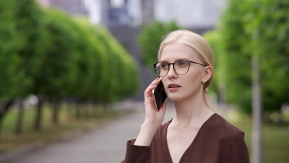 Young Business Woman Answers the Phone and Talks on the Phone with a Colleague at Work