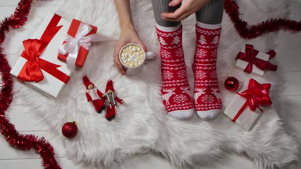 Woman in Warm Red White Socks with an Ornament Sits on a Fur Skin Around Boxes with Gifts and New alt