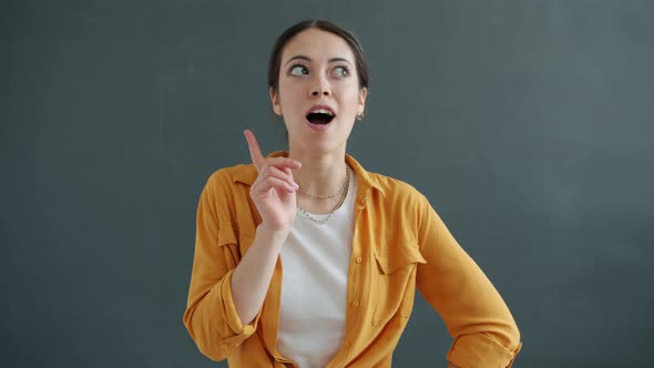 Slow Motion Portrait of Pensive Lady Raising Forefinger Having Great Idea Smiling alt
