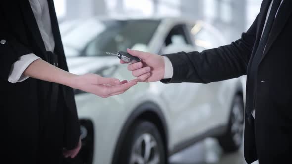 Close-up of Male Caucasian Dealer Giving Car Keys To Unrecognizable Young Woman in Suit alt